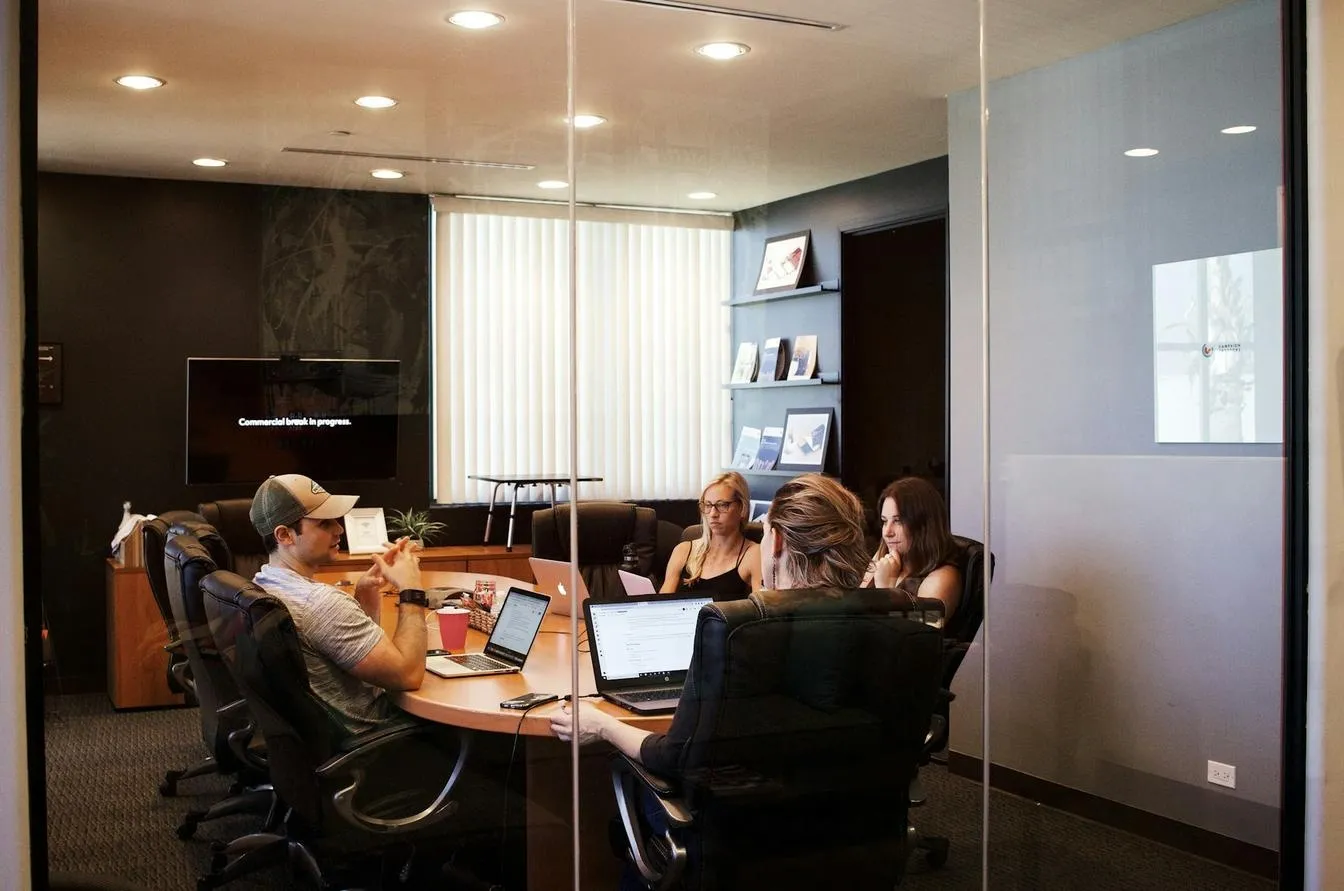 Team of professionals in a modern office meeting room, collaborating with laptops around a conference table.