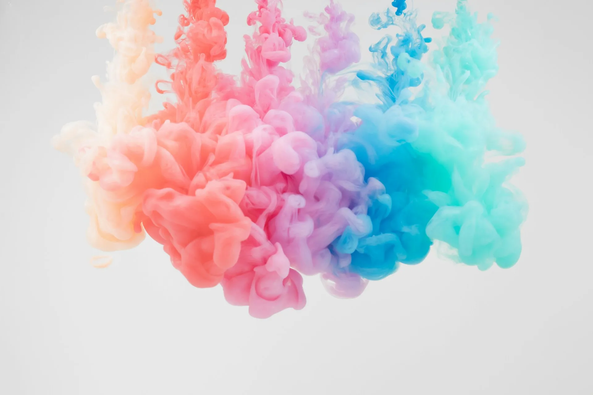 Colourful ink clouds blending from pink to blue in water against a light background.