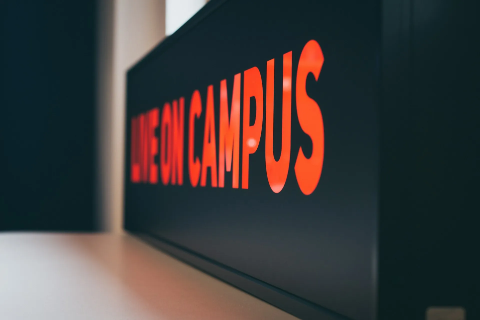 Close-up of a bold red neon sign reading “Live on Campus” against a dark background.