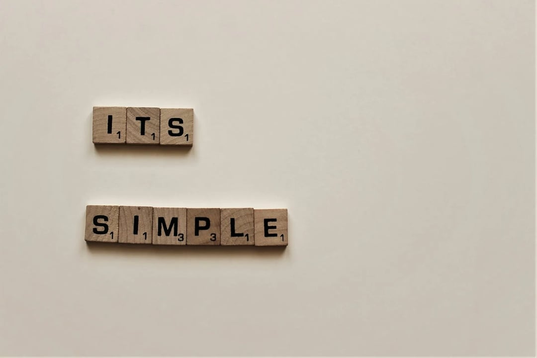 Wooden letter tiles arranged on a plain surface spelling out the phrase 'ITS SIMPLE' in two lines.