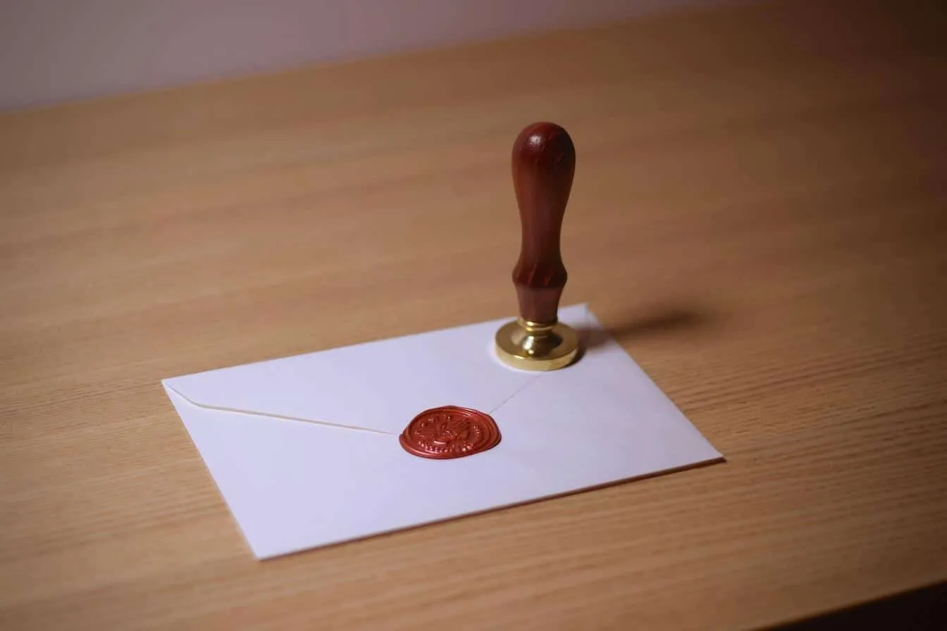 An envelope sealed with a red wax stamp and a wooden sealing stamp resting beside it on a wooden surface.