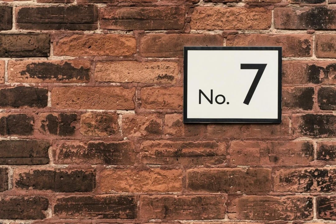 A white rectangular sign framed in black is mounted on a red brick wall.