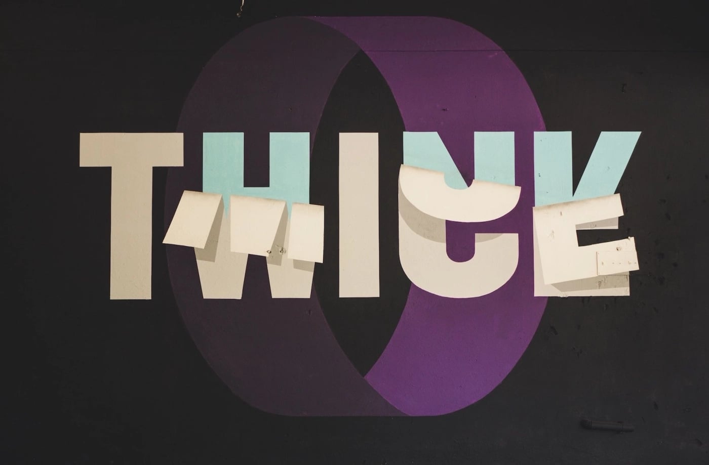 Street art typography mural displaying the word "THINK" in bold, block letters with a 3D illusion and torn paper effect, set against a dark background with purple and blue elements.