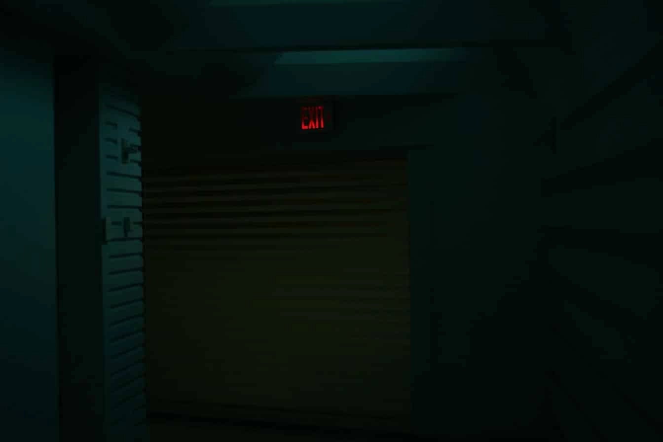 Dimly lit hallway with red exit sign symbolising alertness, system security, and risk awareness.