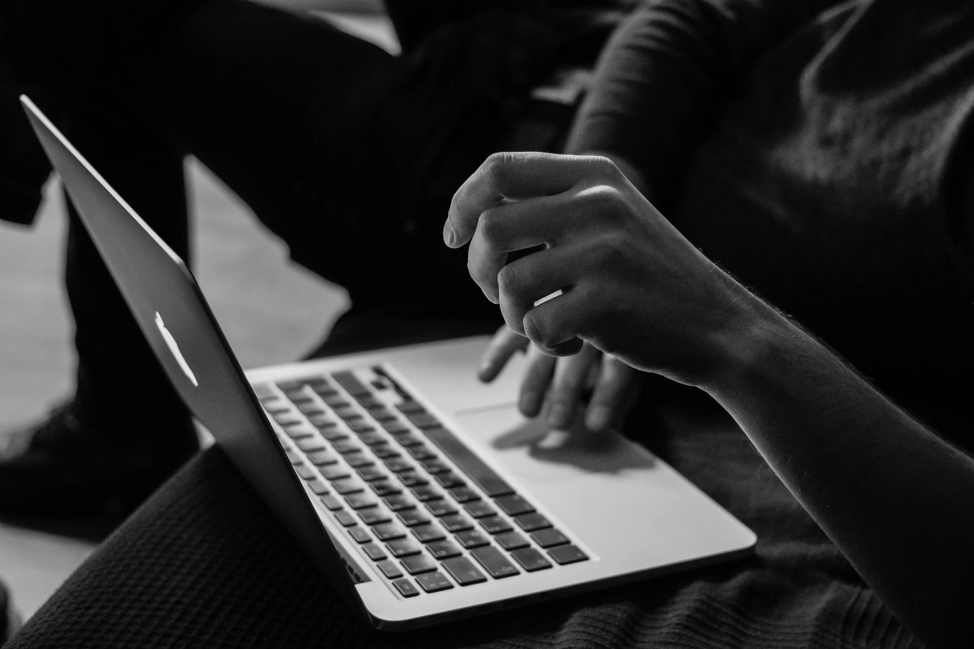 Black and white close-up of a person using a laptop, with hands actively typing and a focused atmosphere.