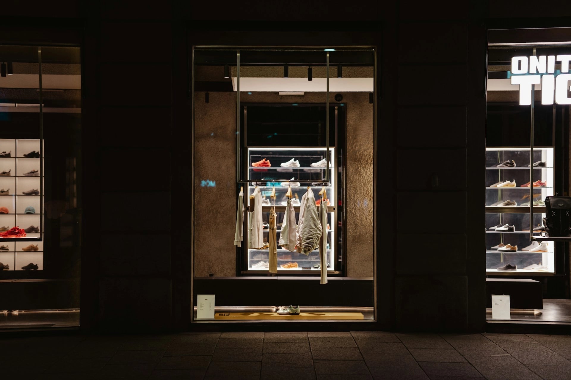 A stylish shoe store display at night, featuring shelves of sneakers and clothing items with illuminated shelves and a modern aesthetic.