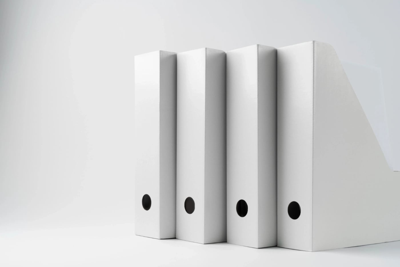 Row of white office binders standing next to a file holder on a plain background.