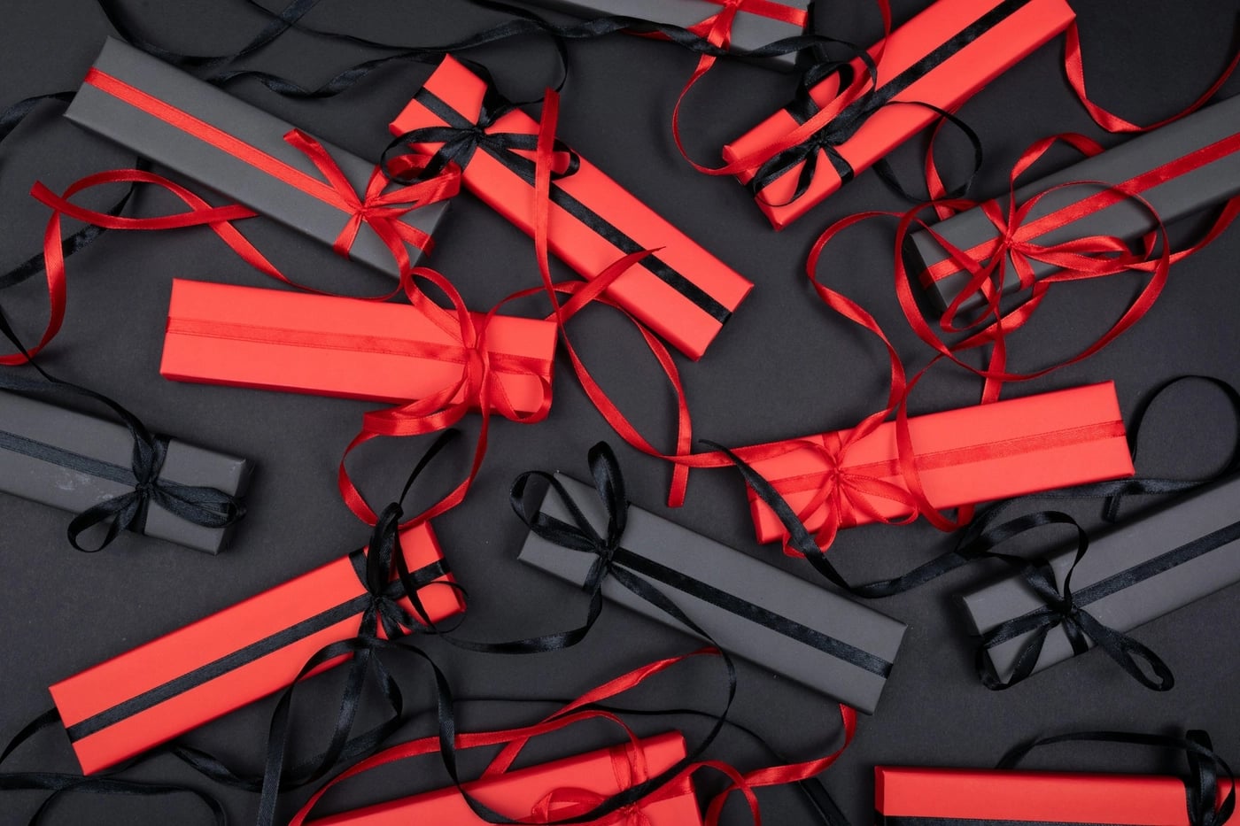 Flat lay of red and black rectangular gift boxes tied with matching satin ribbons on a dark background.