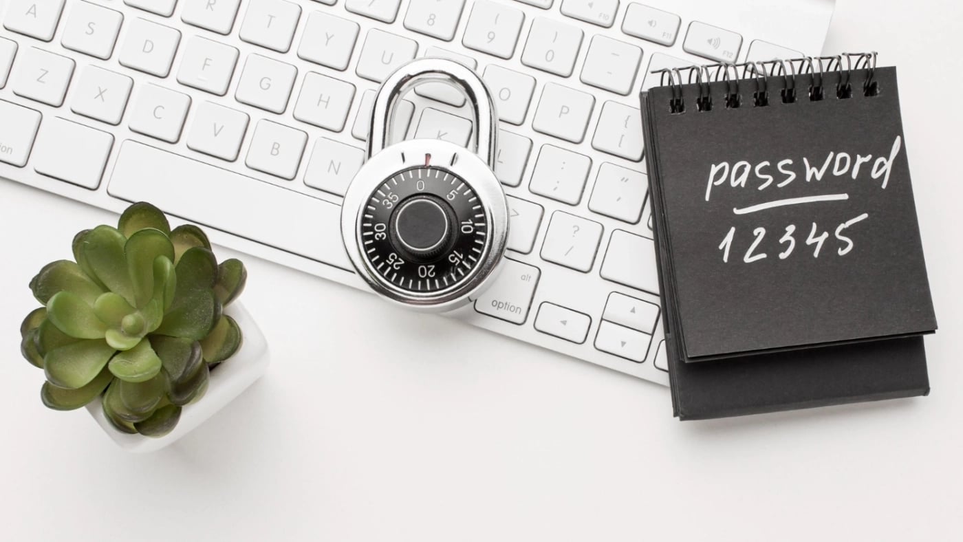 Notebook with "password 12345" written on it, placed on a white keyboard next to a padlock and a small green succulent plant - symbolizing weak password security.