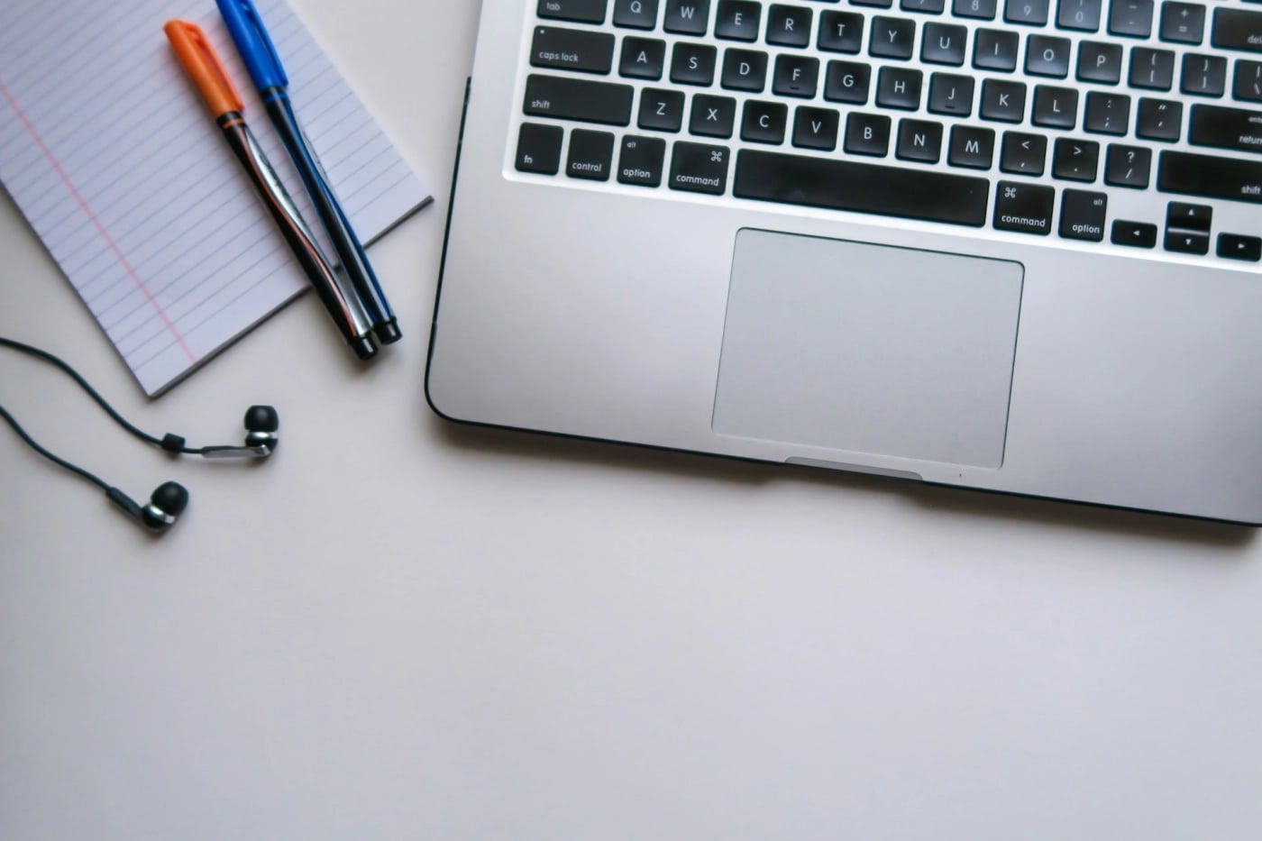 Close-up of a laptop with notepad, pens, and earphones on a desk, representing a working environment for digital projects.