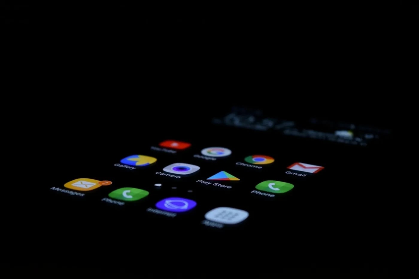 Smartphone screen displaying app icons including Messages, Camera, Play Store, Chrome, Gmail, and Phone in a dark environment.