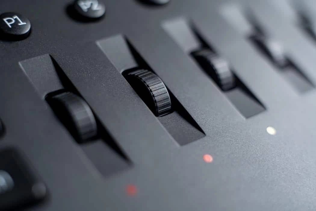 Close-up of black rotary knobs and sliders on a professional audio mixer or sound control panel.