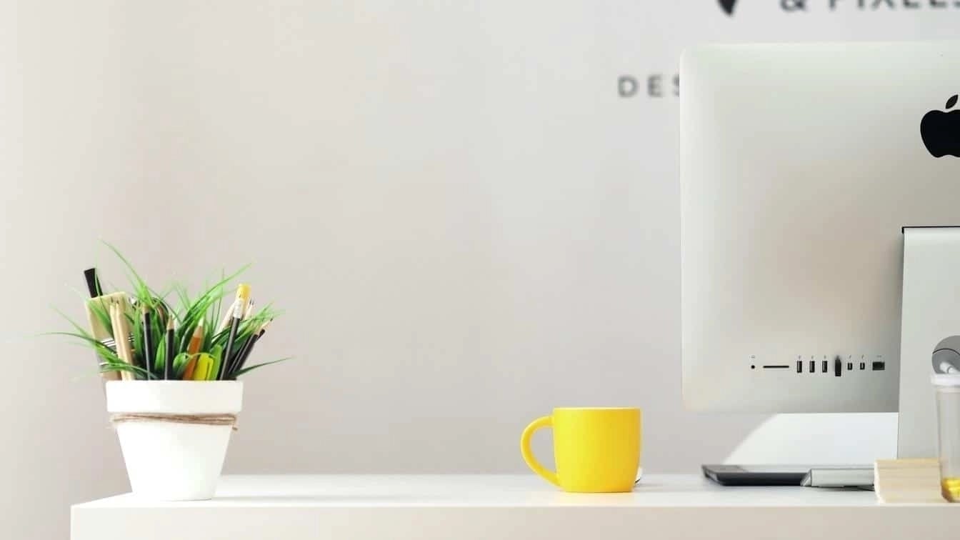 Minimal desk with iMac, yellow mug, and pencil holder symbolising creativity and digital work.