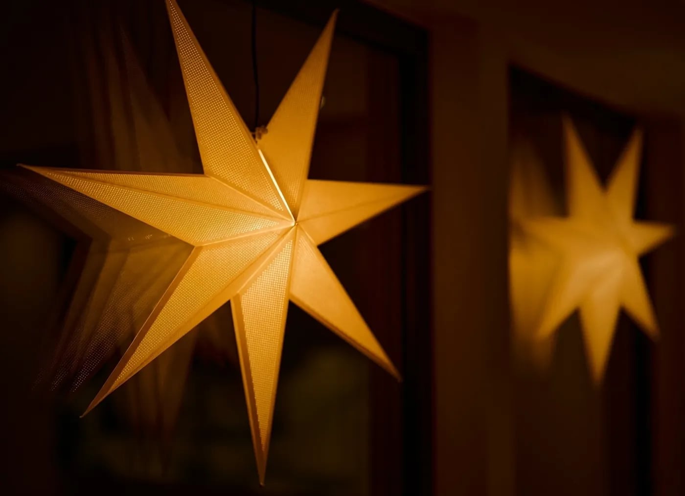 Warmly lit decorative star-shaped lamp hanging indoors with its reflection visible on a nearby window.