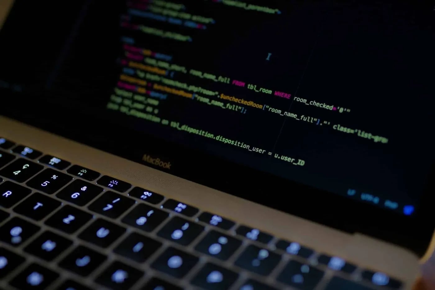 Close-up of a MacBook keyboard and screen displaying code in a dark-themed text editor.