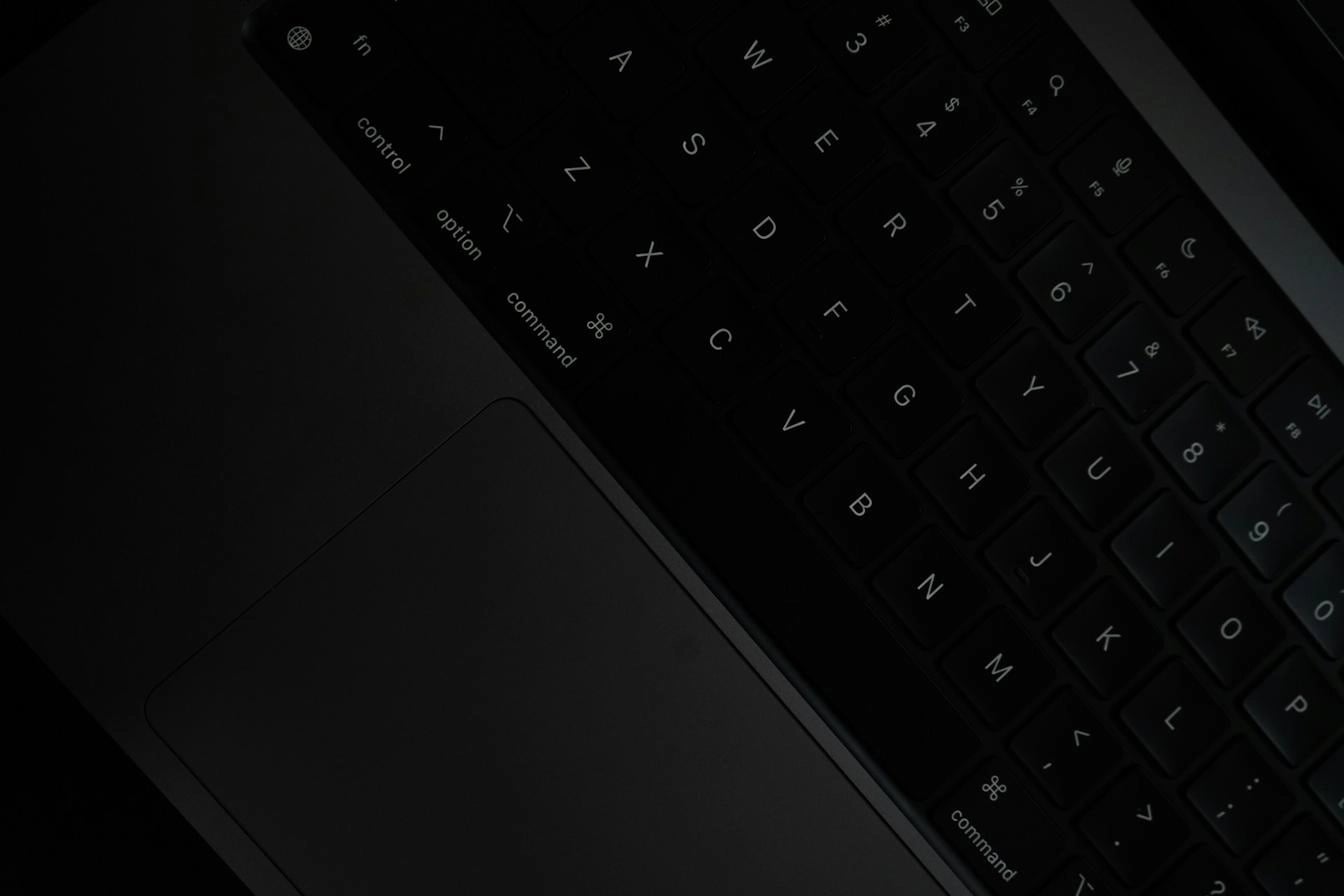 Close-up of a MacBook keyboard and trackpad in low light.