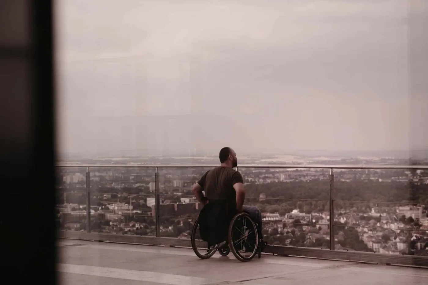 Man in a wheelchair gazing over a city skyline from a glass observation deck, symbolising independence and accessibility.
