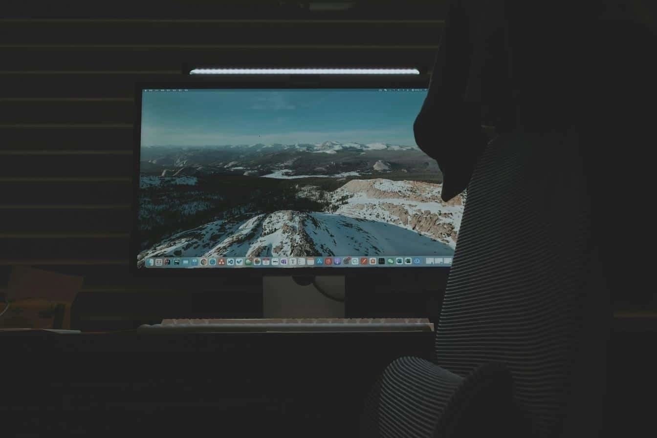 Dark office setup with a computer screen displaying snowy mountain landscape and a keyboard.