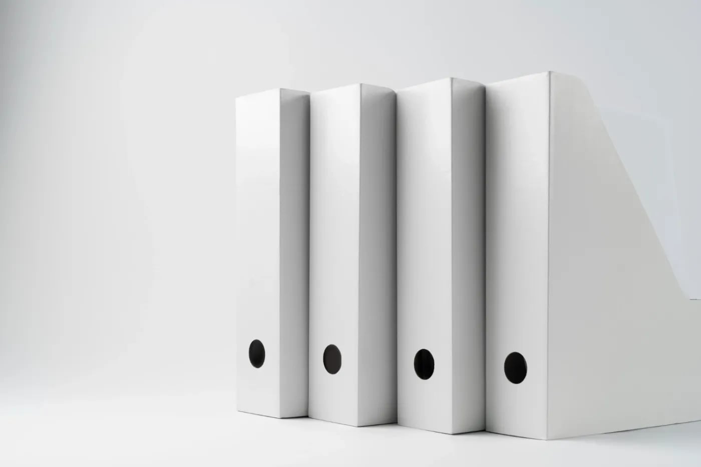 Row of white office binders standing next to a file holder on a plain background.
