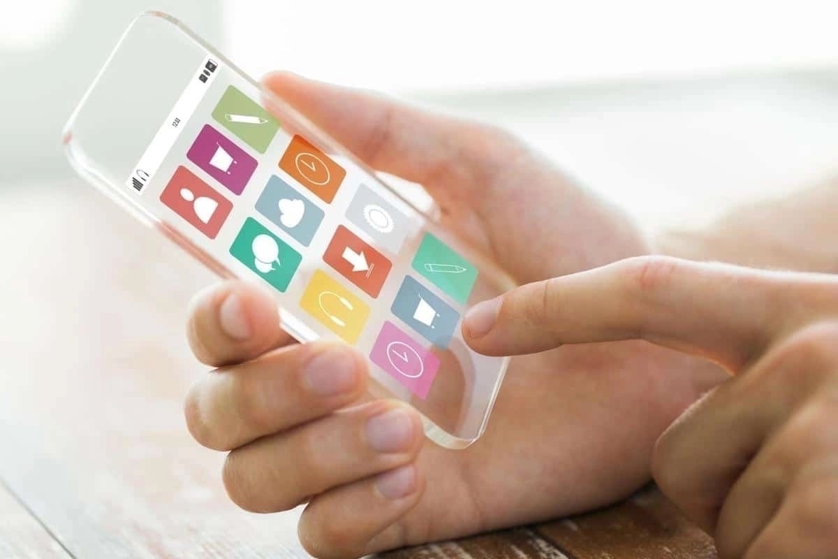 Close-up of a hand holding a smartphone while tapping on a screen displaying colorful square app icons.