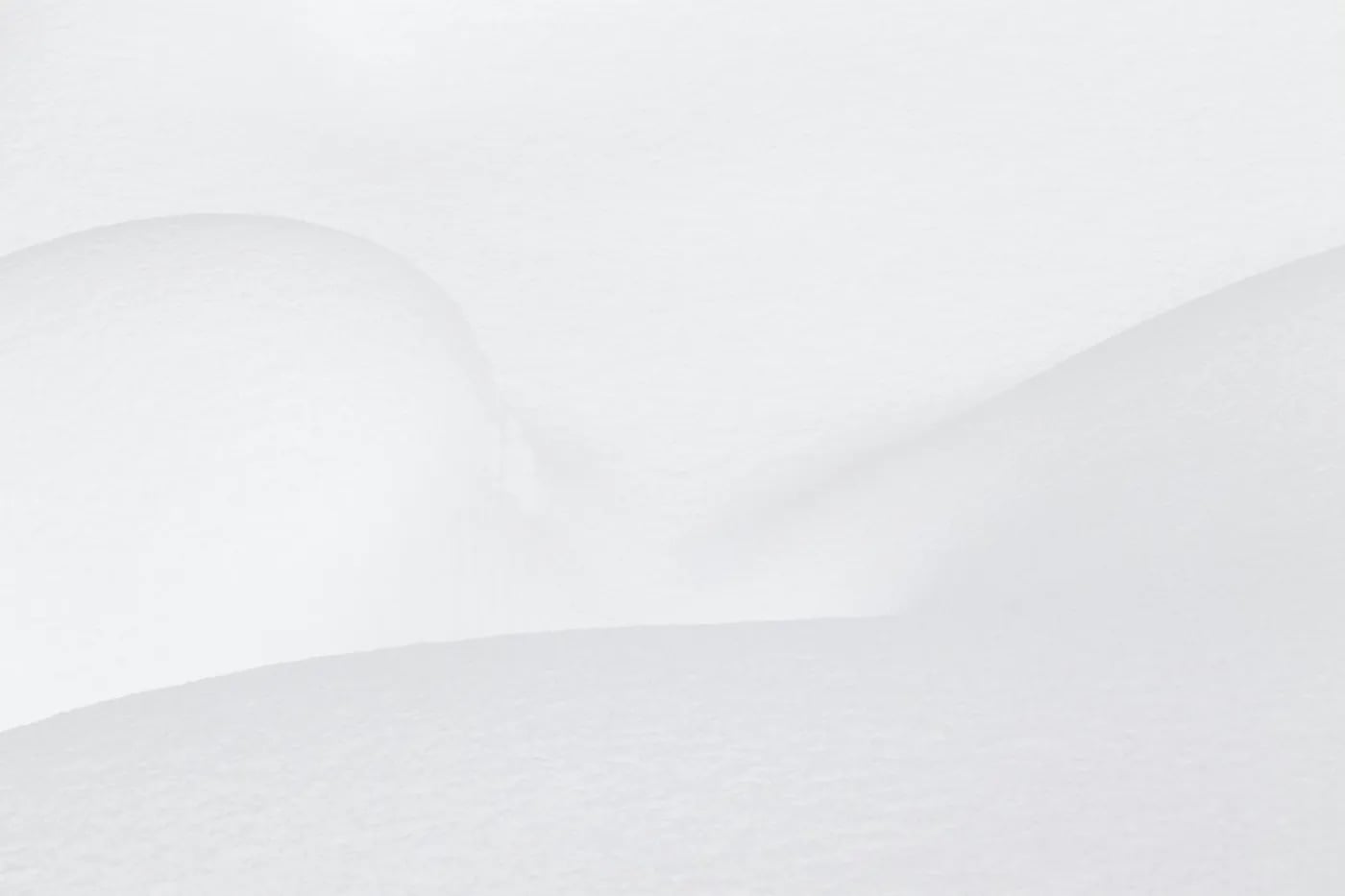 A minimalist image showing smooth, gently curving snowdrifts with a uniform white texture.