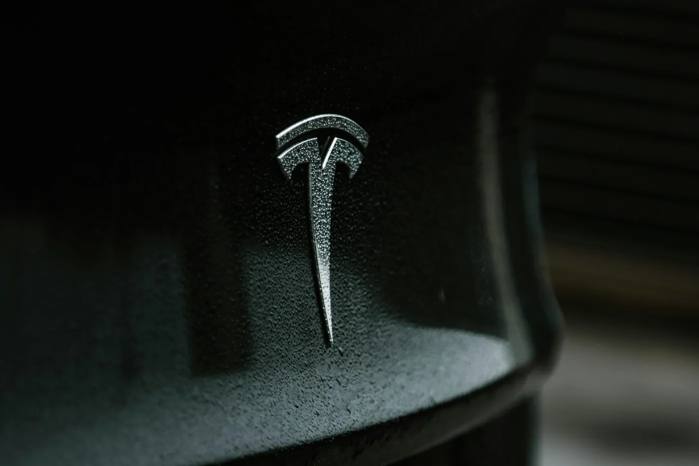 Close-up of the Tesla logo on a glossy black surface with water droplets.