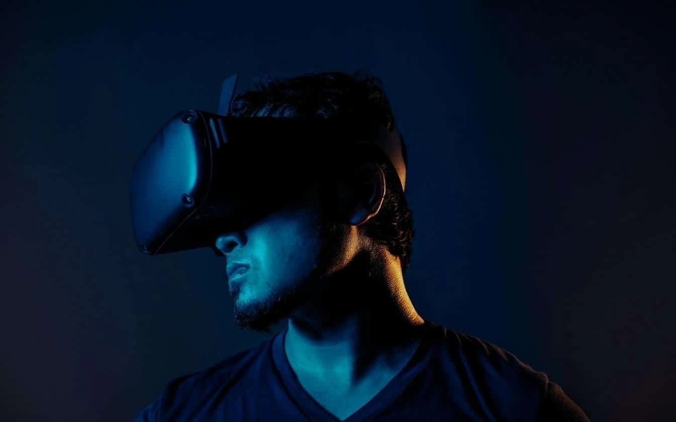 Person wearing a VR headset under dramatic blue lighting, facing sideways against a dark background.