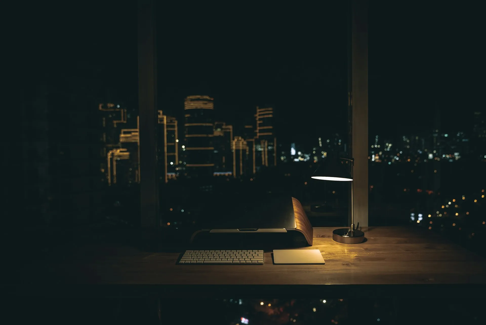 Minimalist desk setup with keyboard, mouse, and desk lamp overlooking a city skyline at night.