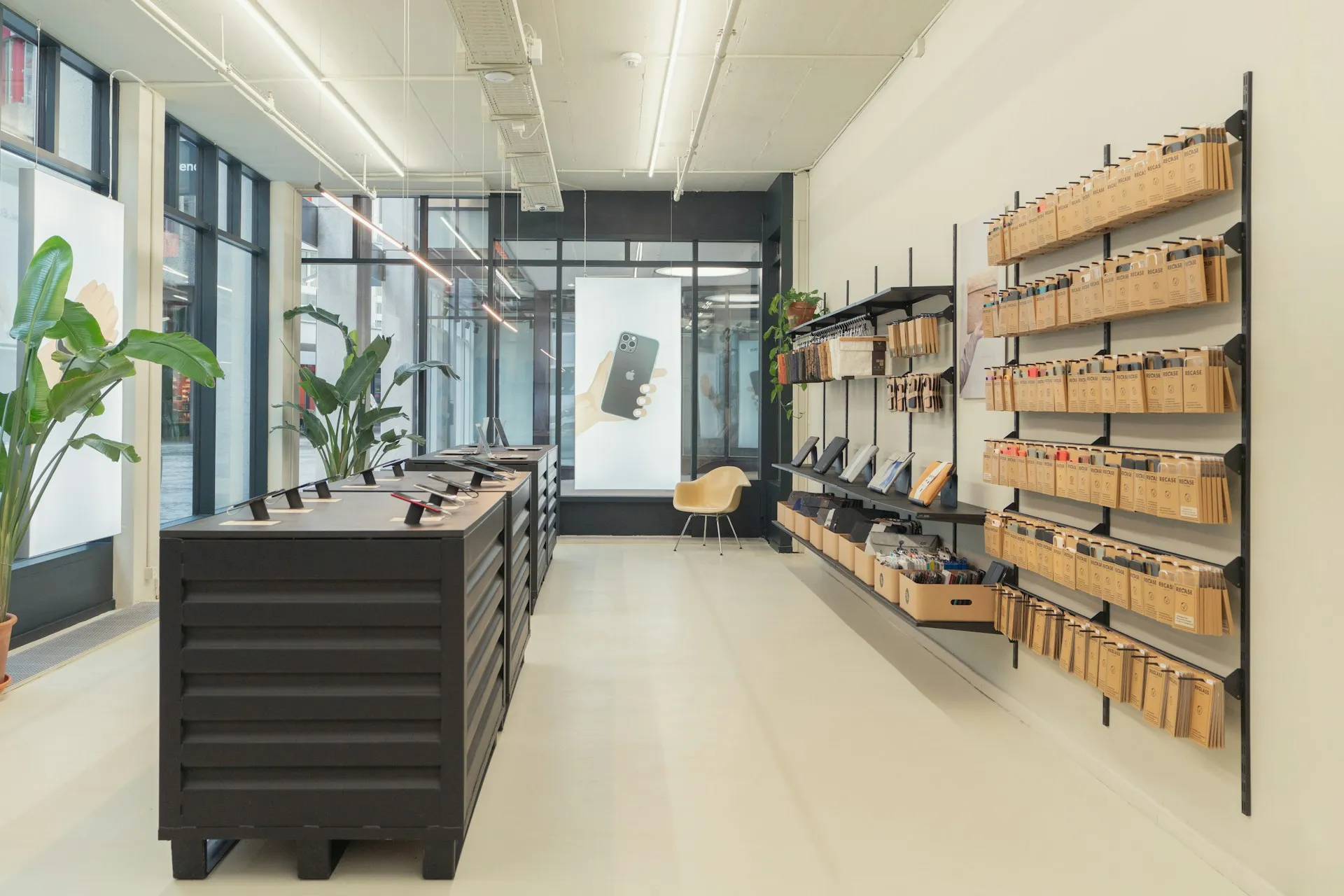 Modern retail store with minimalist interior, displaying tech accessories and phone cases on wall-mounted shelves, with tablets on central black counters.