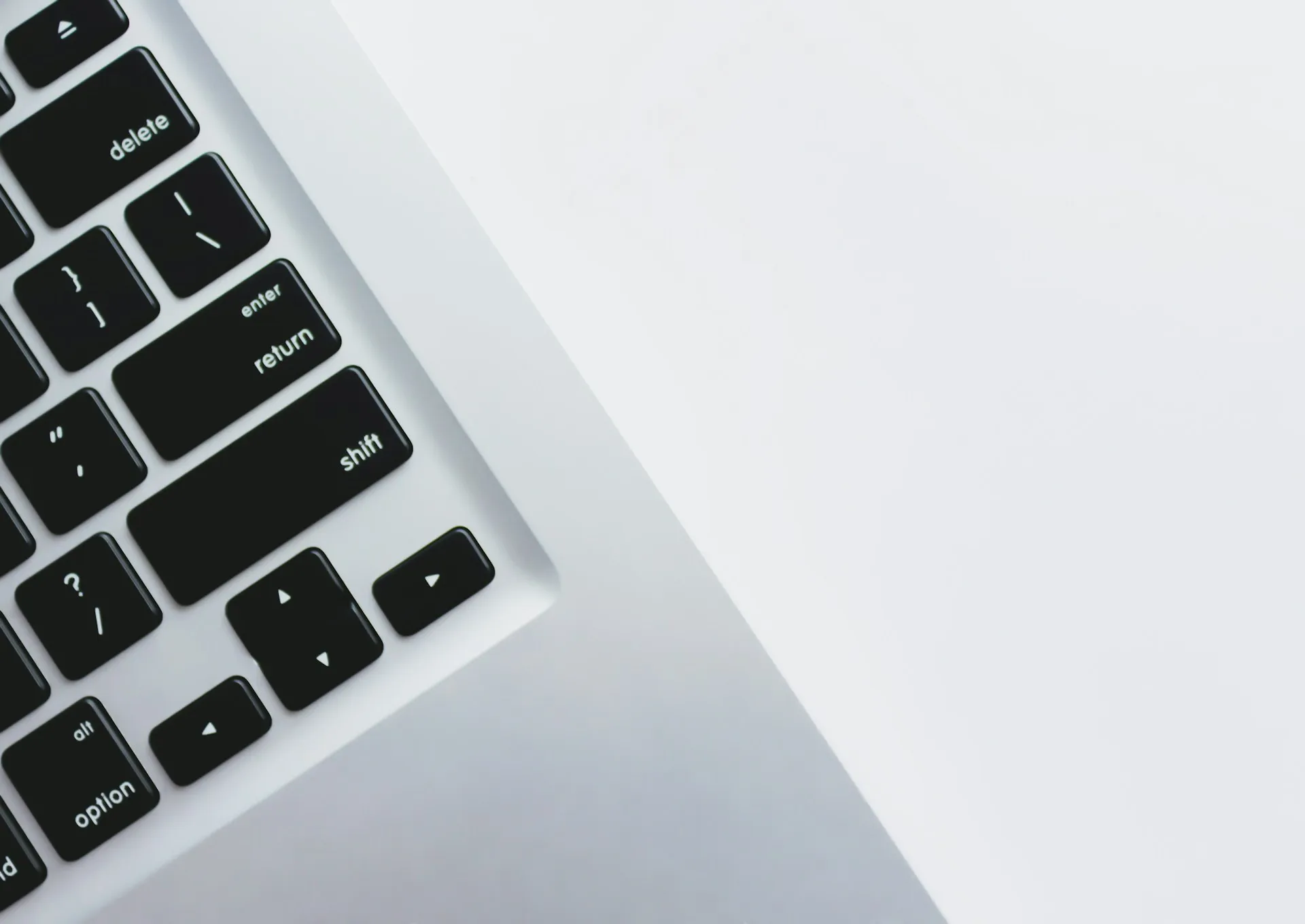 Close-up of a black and white laptop keyboard, focusing on the return, shift, and arrow keys, with a minimal white background.