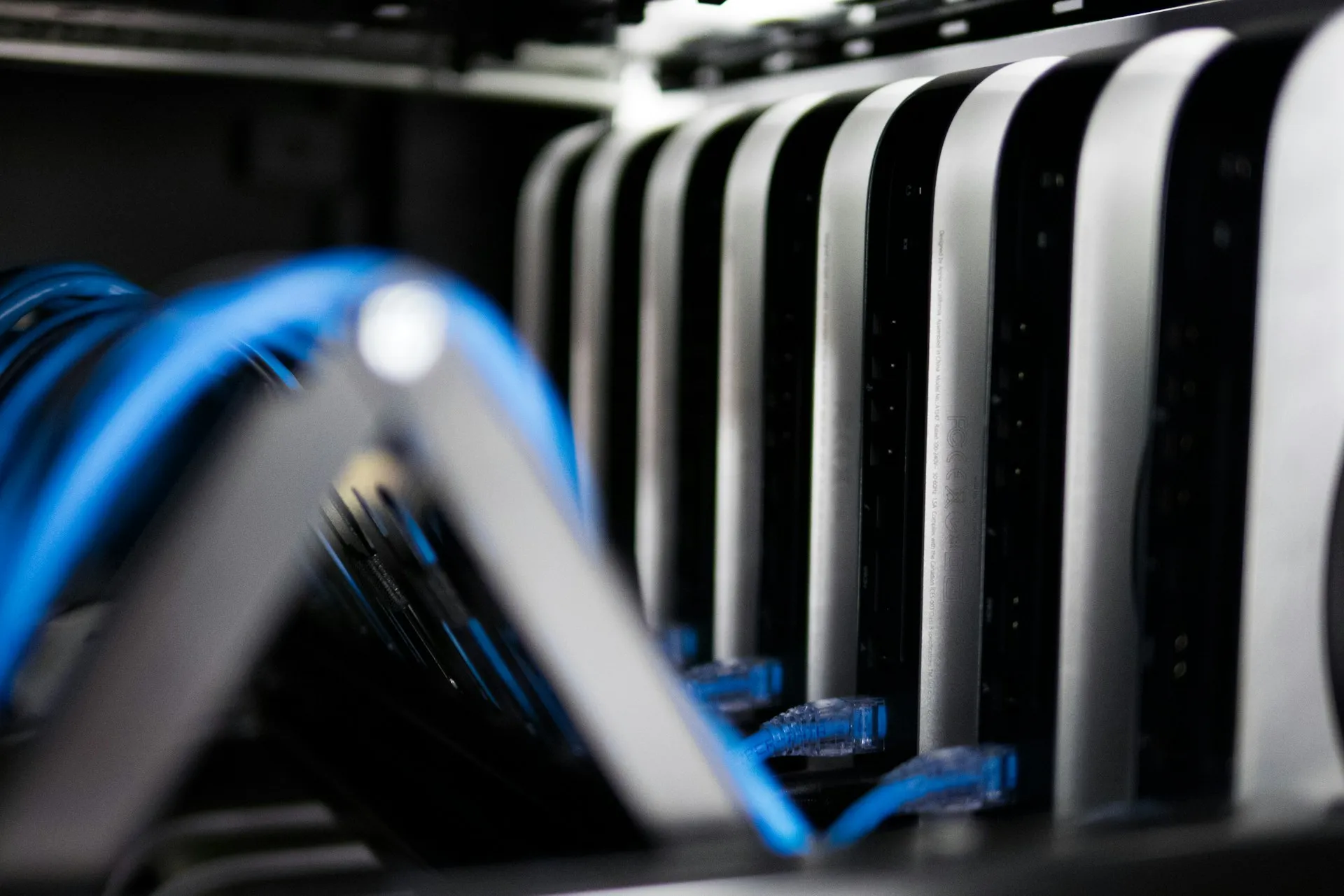 Close-up of multiple networked Mac Mini servers connected with blue Ethernet cables in a data center rack.