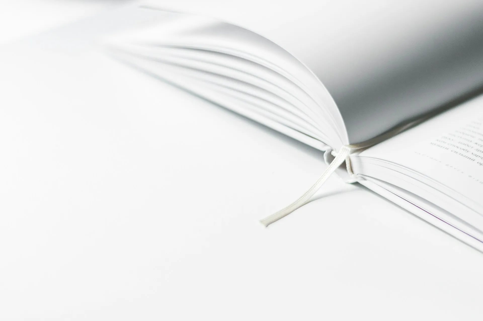 Close-up of an open book with a ribbon bookmark on a white background.