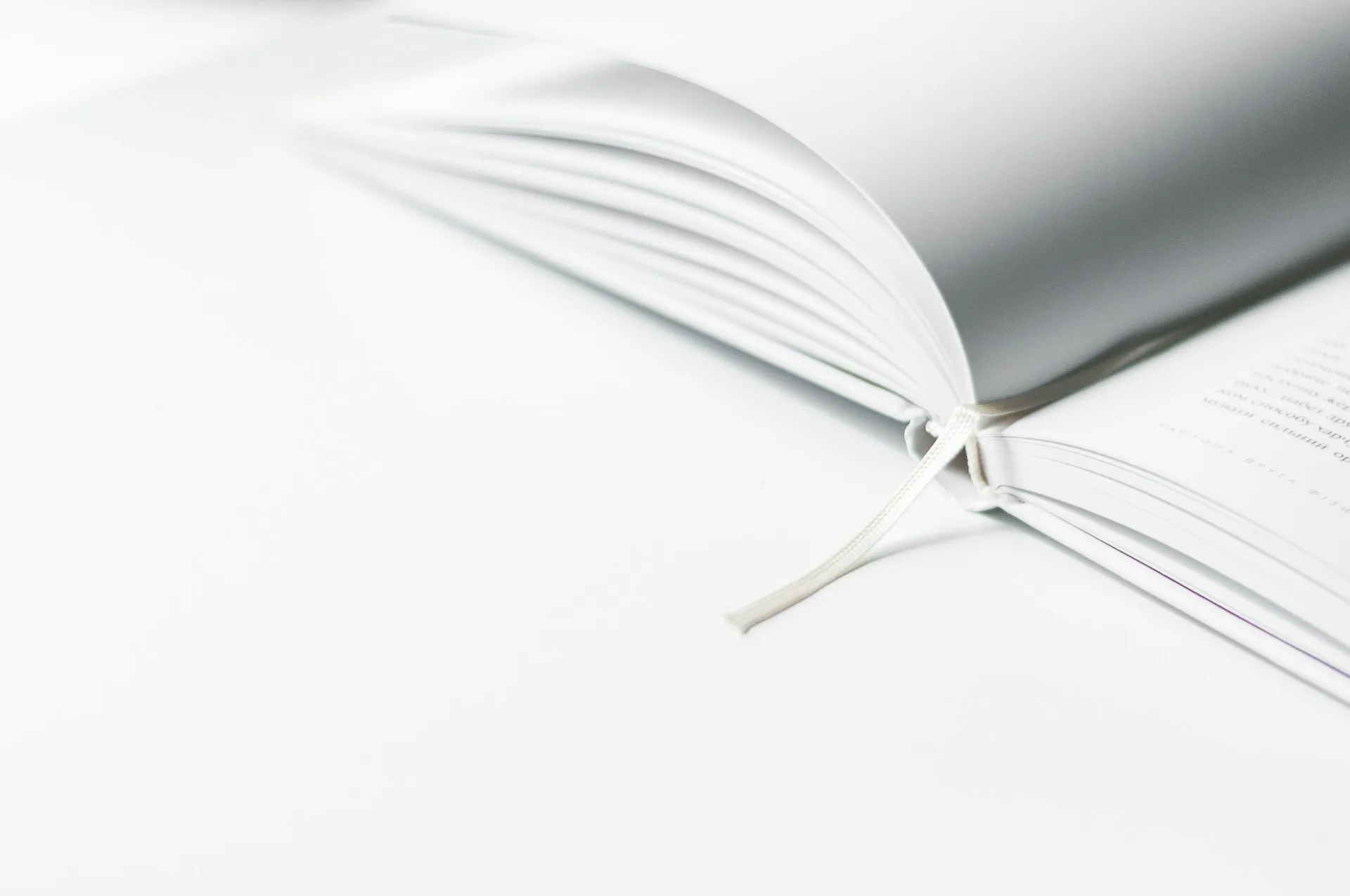 Close-up of an open book with a ribbon bookmark on a white background.