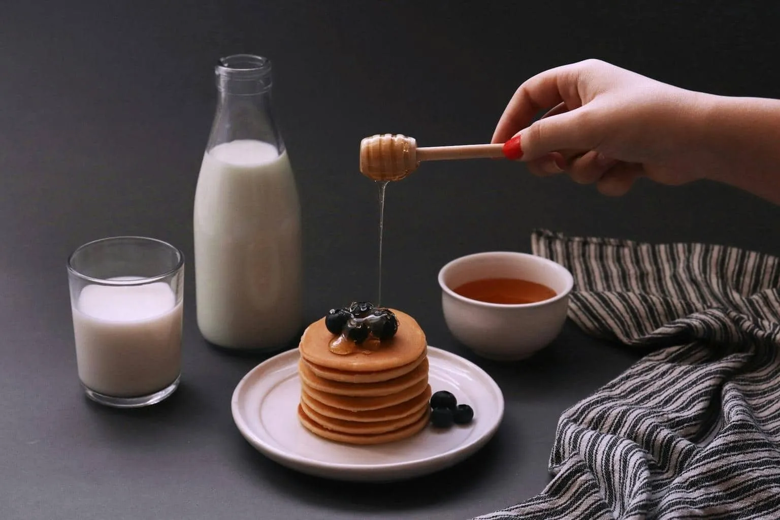 Pancakes with blueberries A stack of pancakes topped with blueberries and honey being drizzled from a wooden honey dipper.