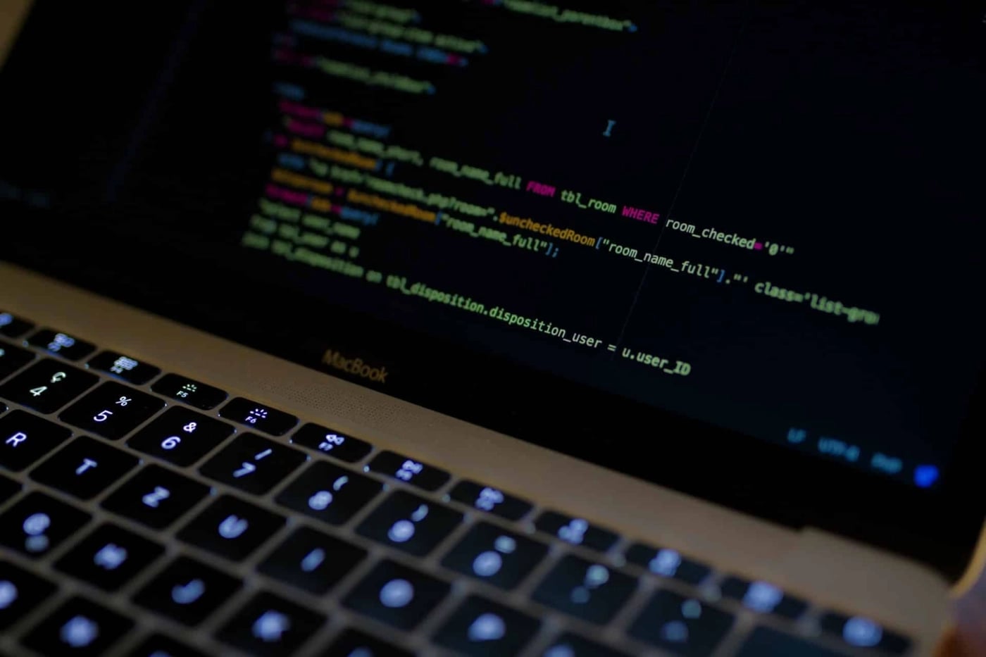 Close-up of a MacBook keyboard and screen displaying code in a dark-themed text editor.