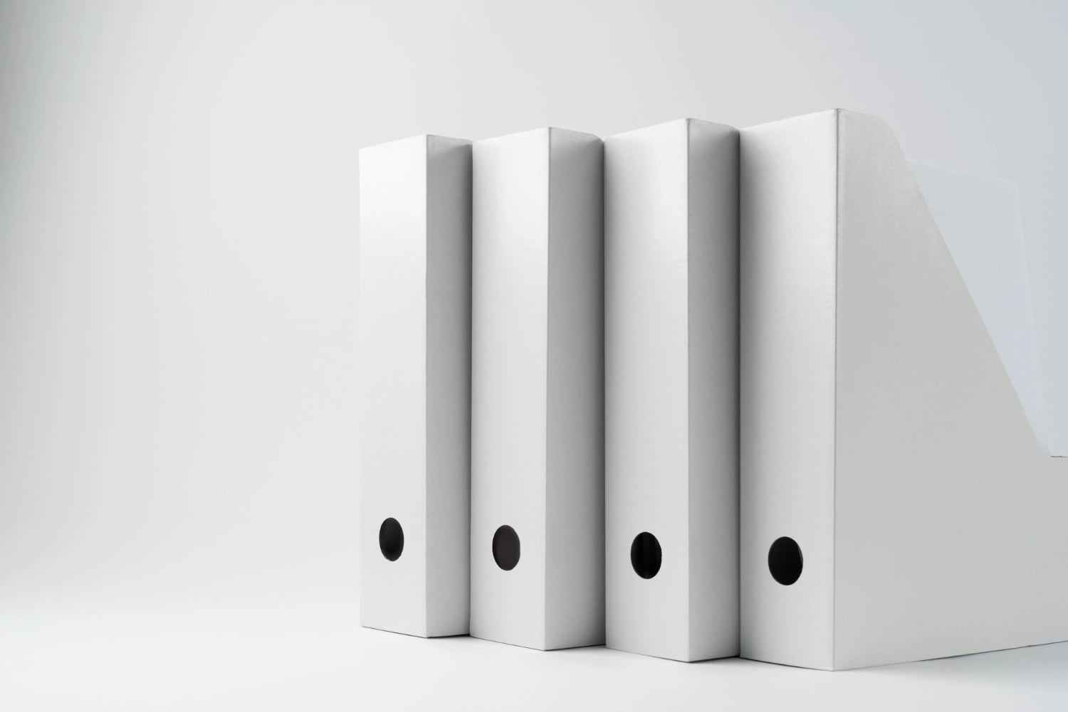 Row of white office binders standing next to a file holder on a plain background.