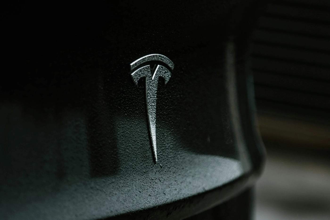Close-up of the Tesla logo on a glossy black surface with water droplets.