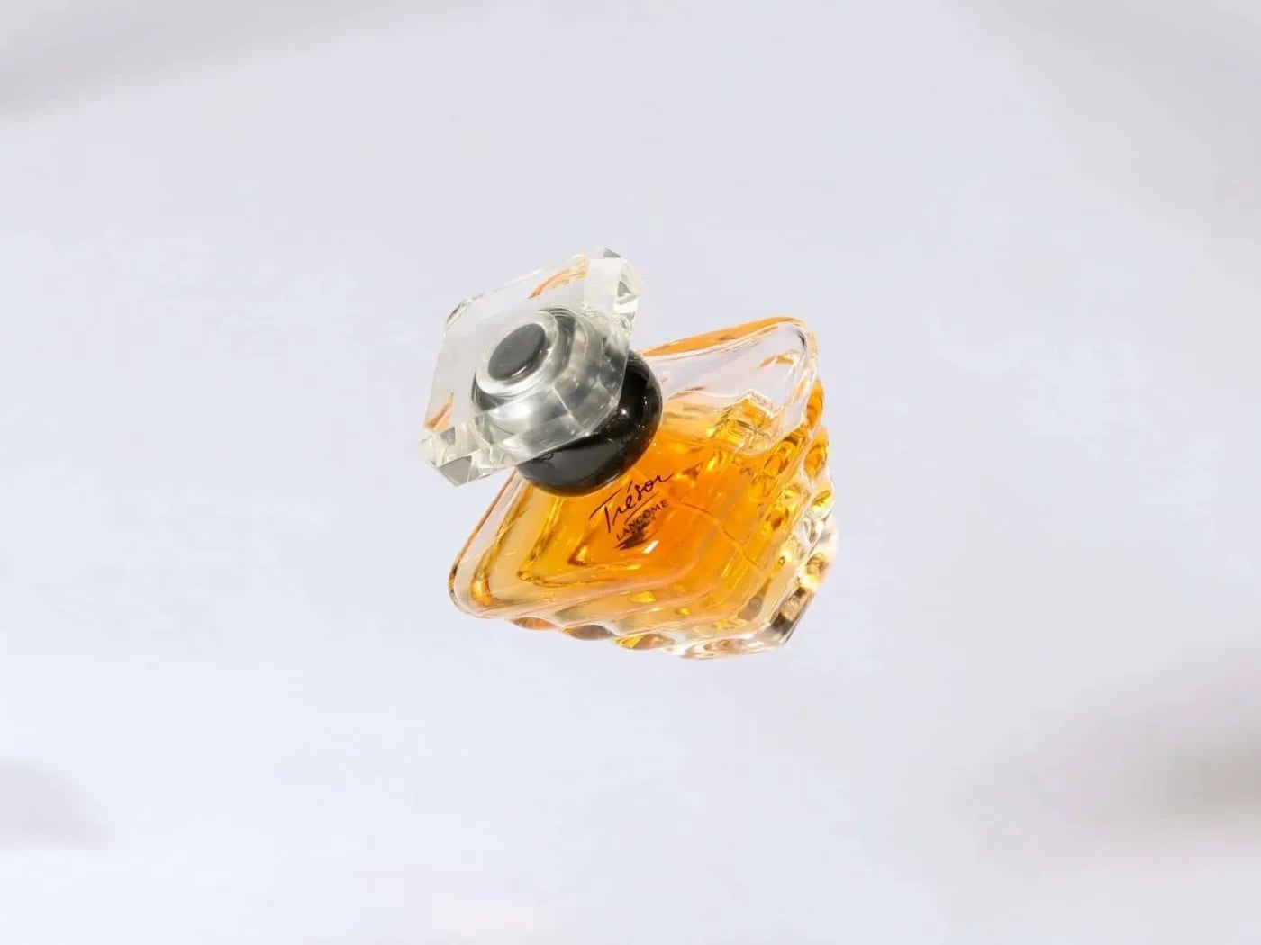 Triangular glass perfume bottle with amber liquid and clear cap floating on white background.