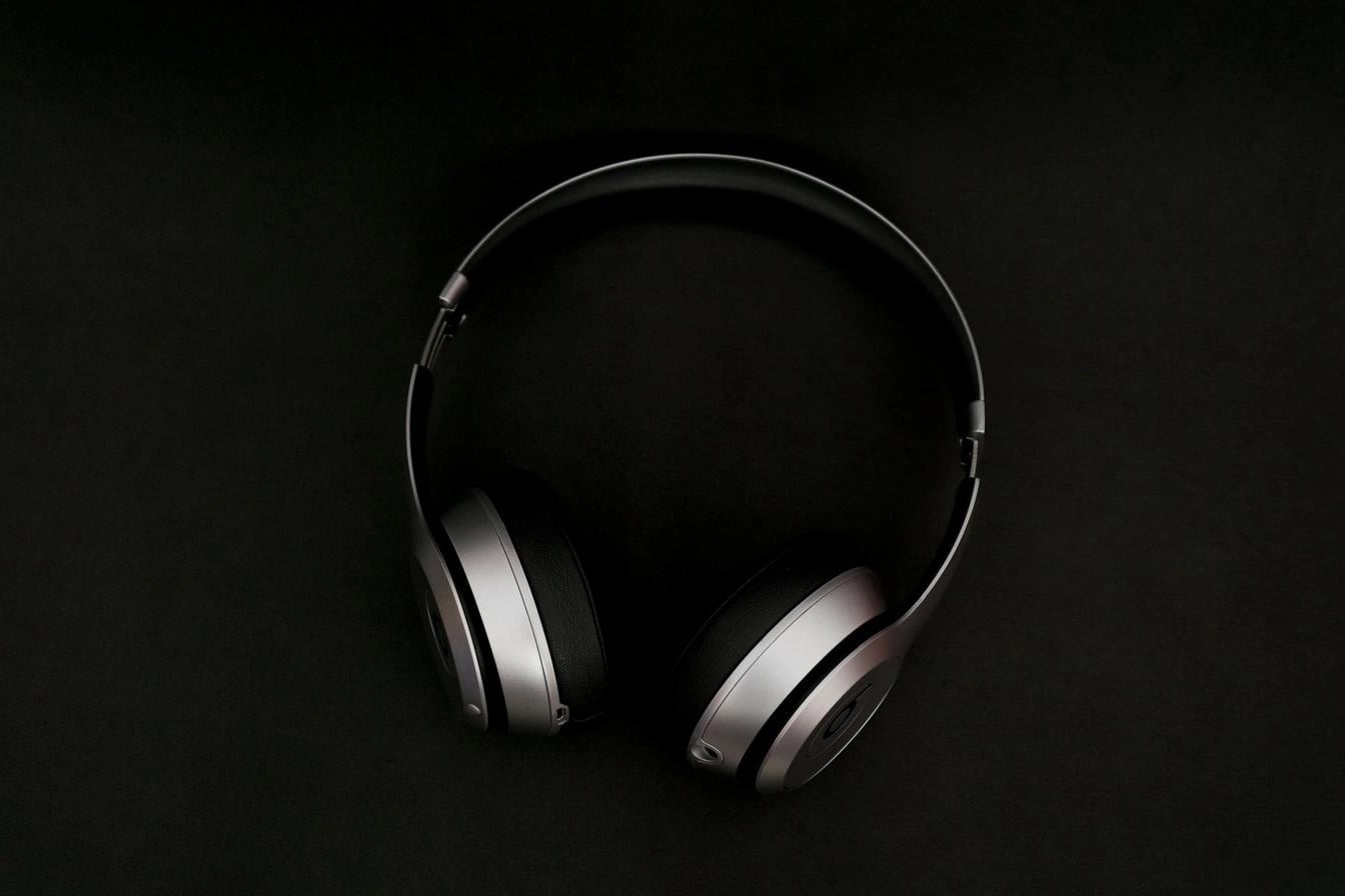 Sleek over-ear headphones in silver and black placed on a matte black background.