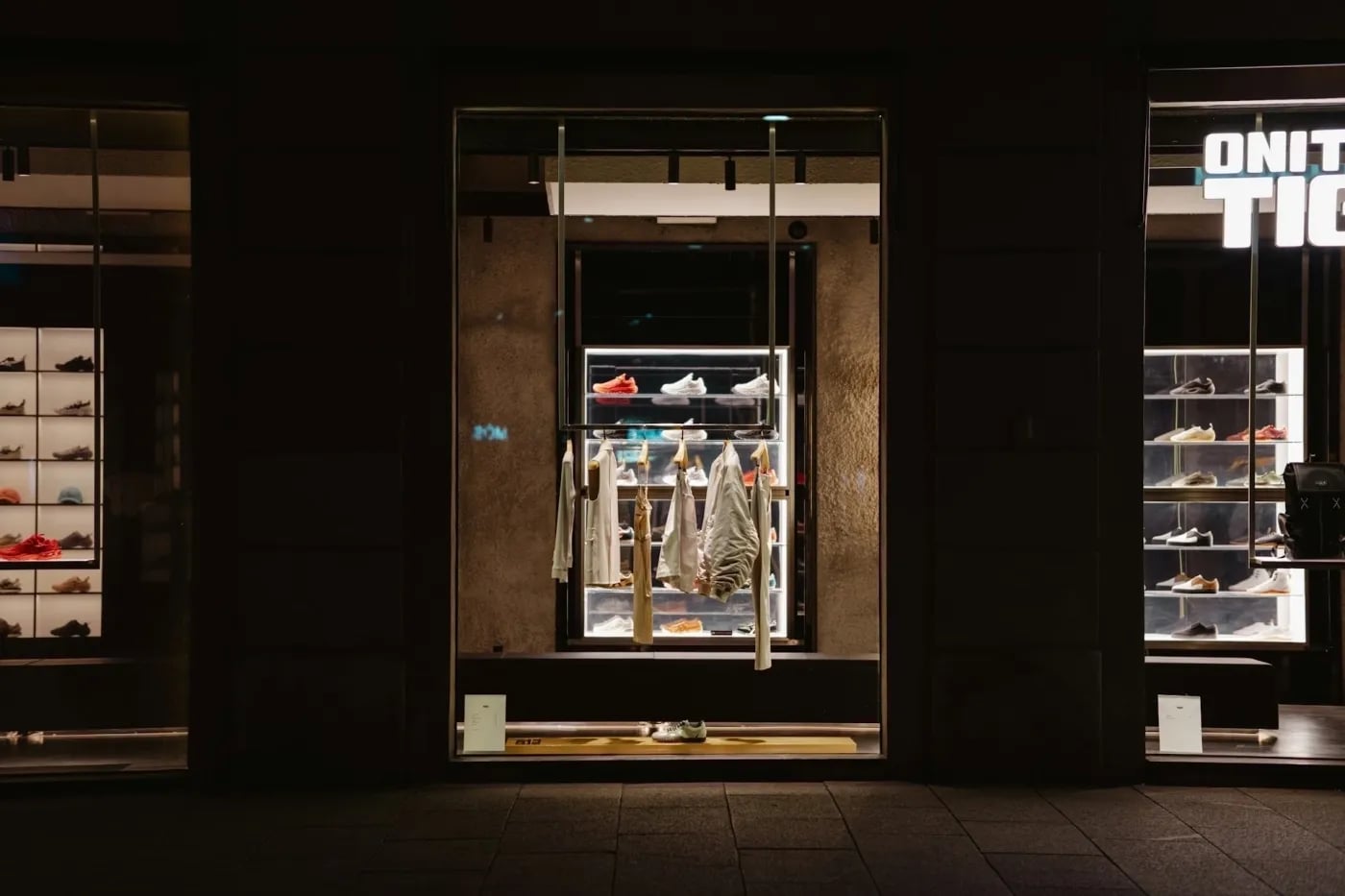 A stylish shoe store display at night, featuring shelves of sneakers and clothing items with illuminated shelves and a modern aesthetic.