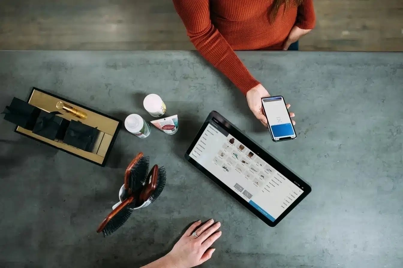 A customer making a contactless payment using a smartphone at a modern retail counter with a digital point-of-sale (POS) system displaying product options.